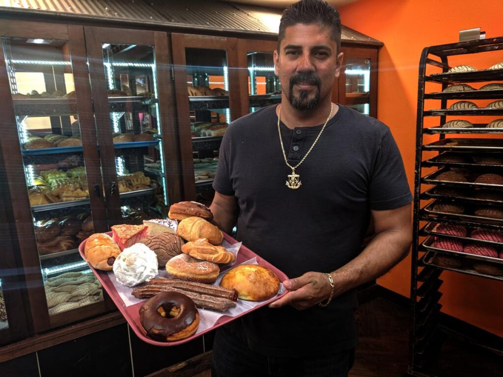 a man holding a tray of donuts in a bakery.