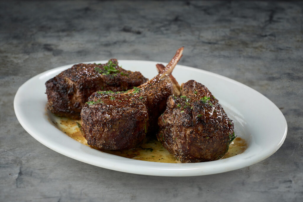 Lamb chops on a plate with sauce on it.