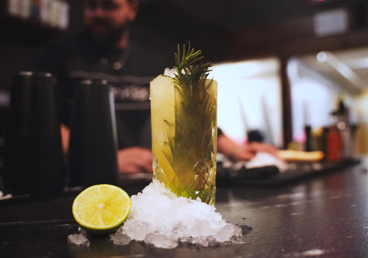 a cocktail with rosemary and ice on top of a bar.