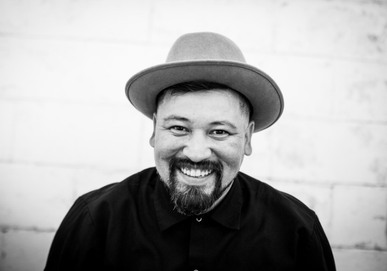 a black and white photo of a smiling man wearing a hat.