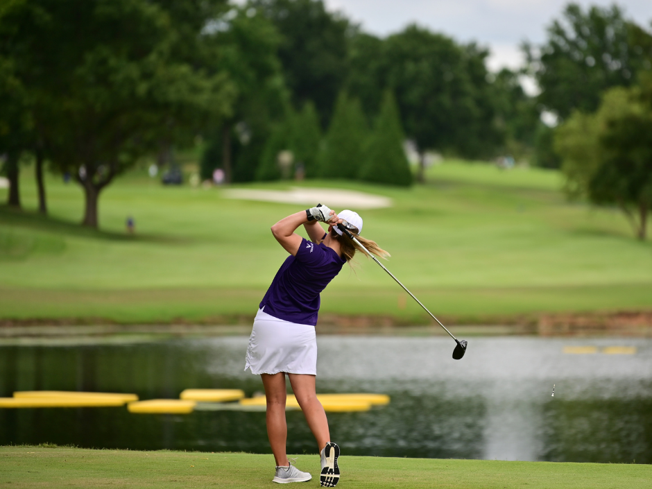 a woman in a purple shirt is hitting a golf ball.