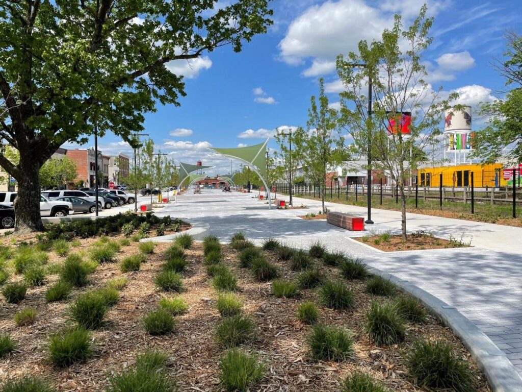 a sidewalk with trees and shrubs in the middle of a city.