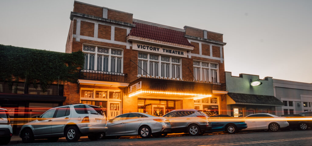 a street scene with cars parked in front of a theater.