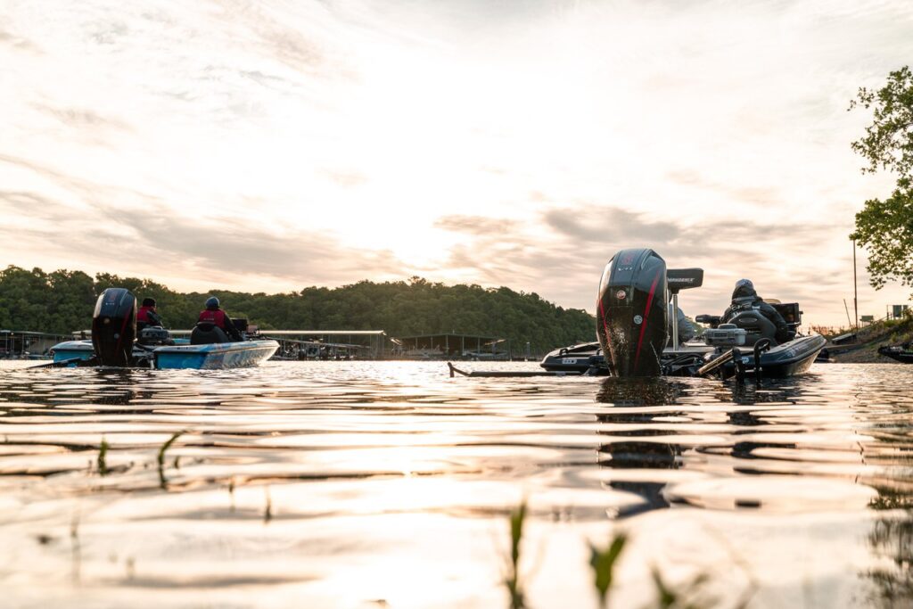 Two bass boats with people on board idling on a lake at sunrise.