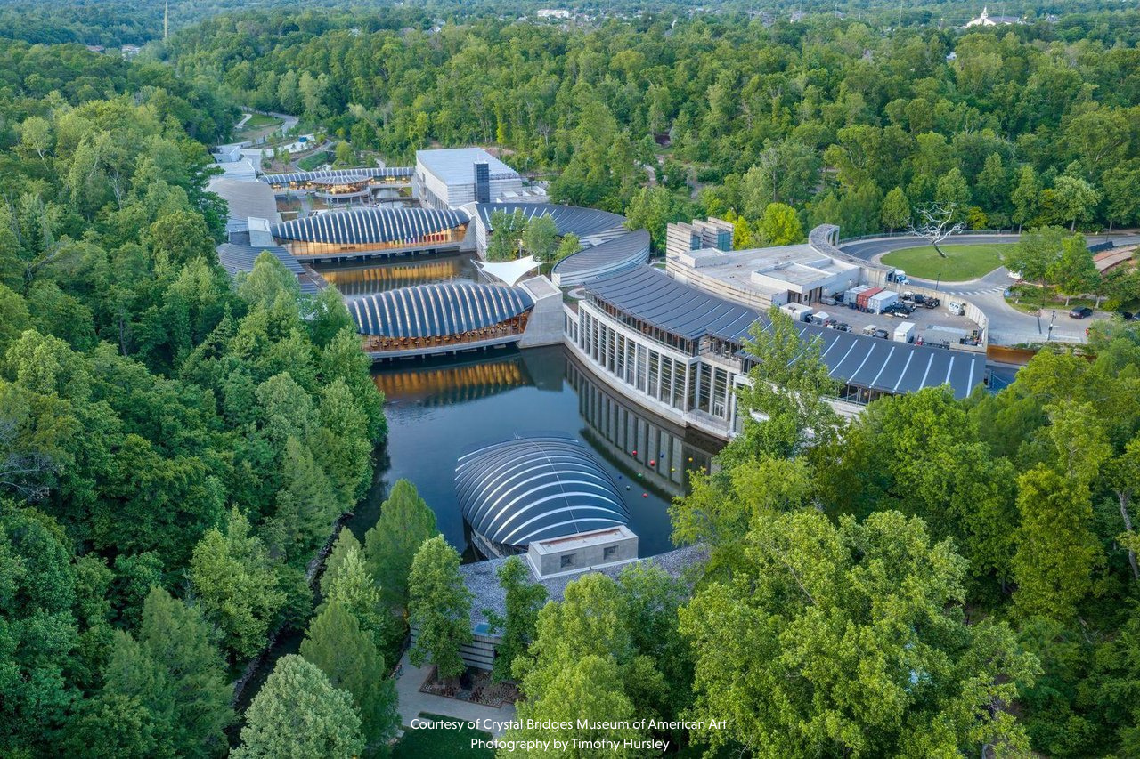 Aerial view of the Crystal Bridges Museum of American Art in Arkansas, featuring modern buildings surrounded by trees and water.