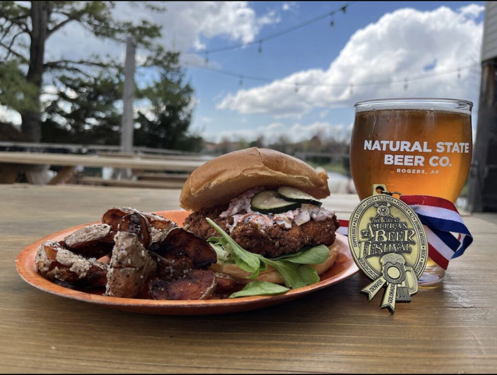 A plate with a burger and a beer on it.