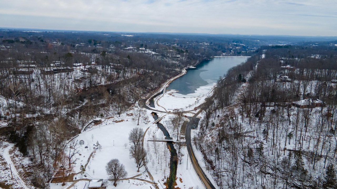 Aerial view of a snowy park with a frozen lake and winding roads surrounded by bare trees.