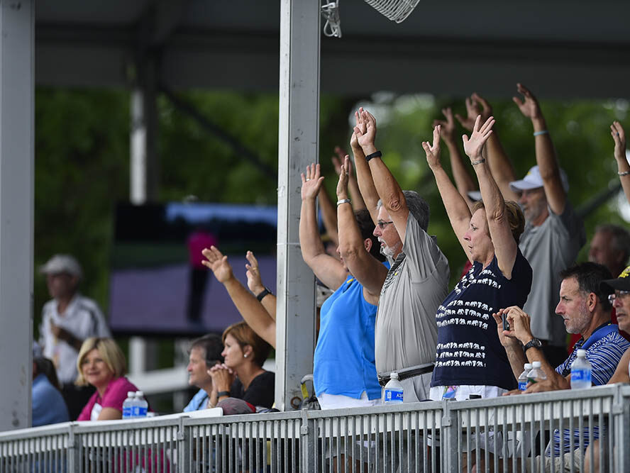 A group of people raising their hands in the stands at a golf tournament.