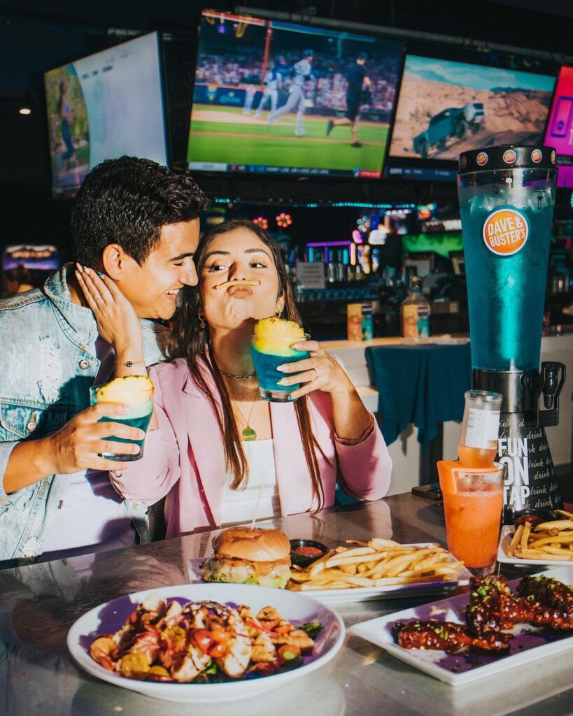 A couple sitting at a table with food and drinks.