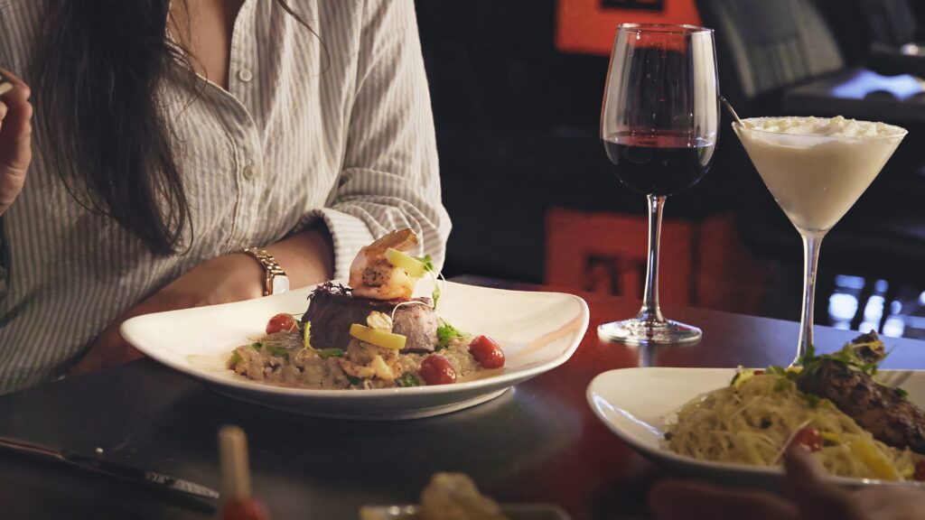 A woman eats a plate of food with a glass of wine.