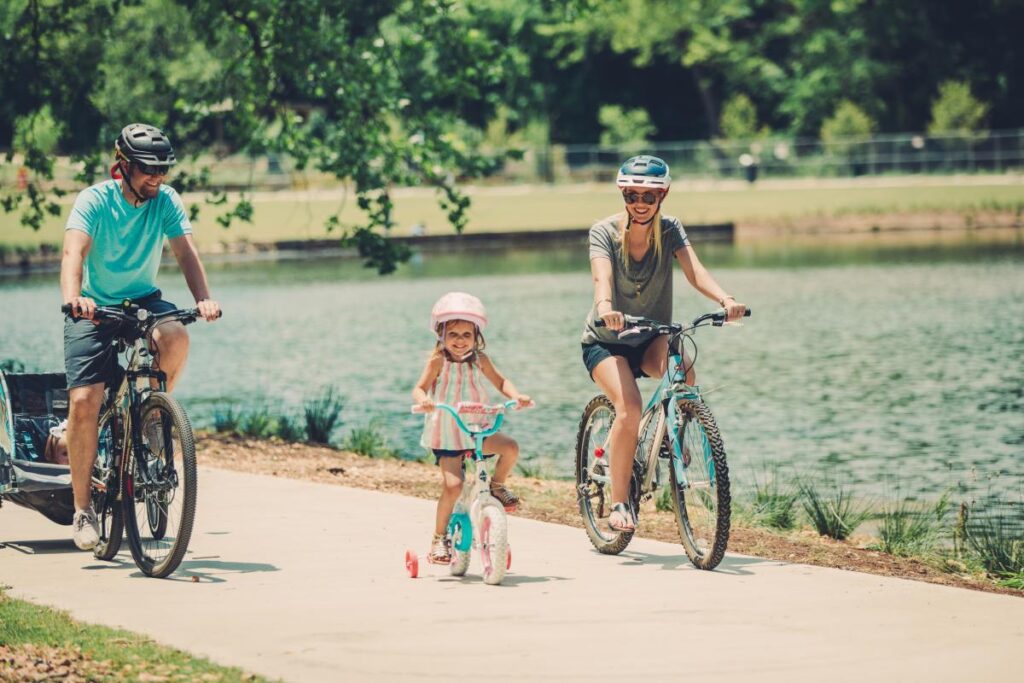 A family is riding bikes on a path near a pond.