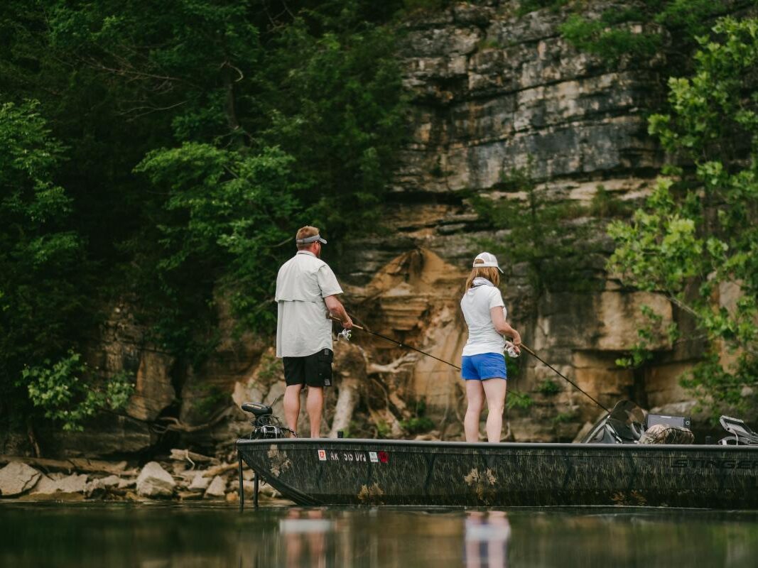 two people fishing on a boat in a rocky area.
