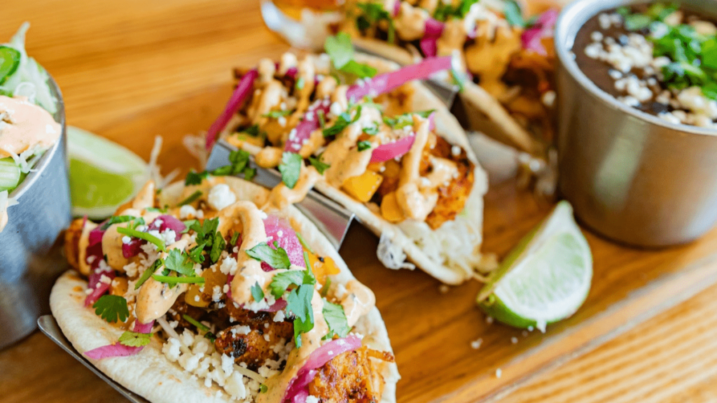 three tacos on a wooden tray with a beer.