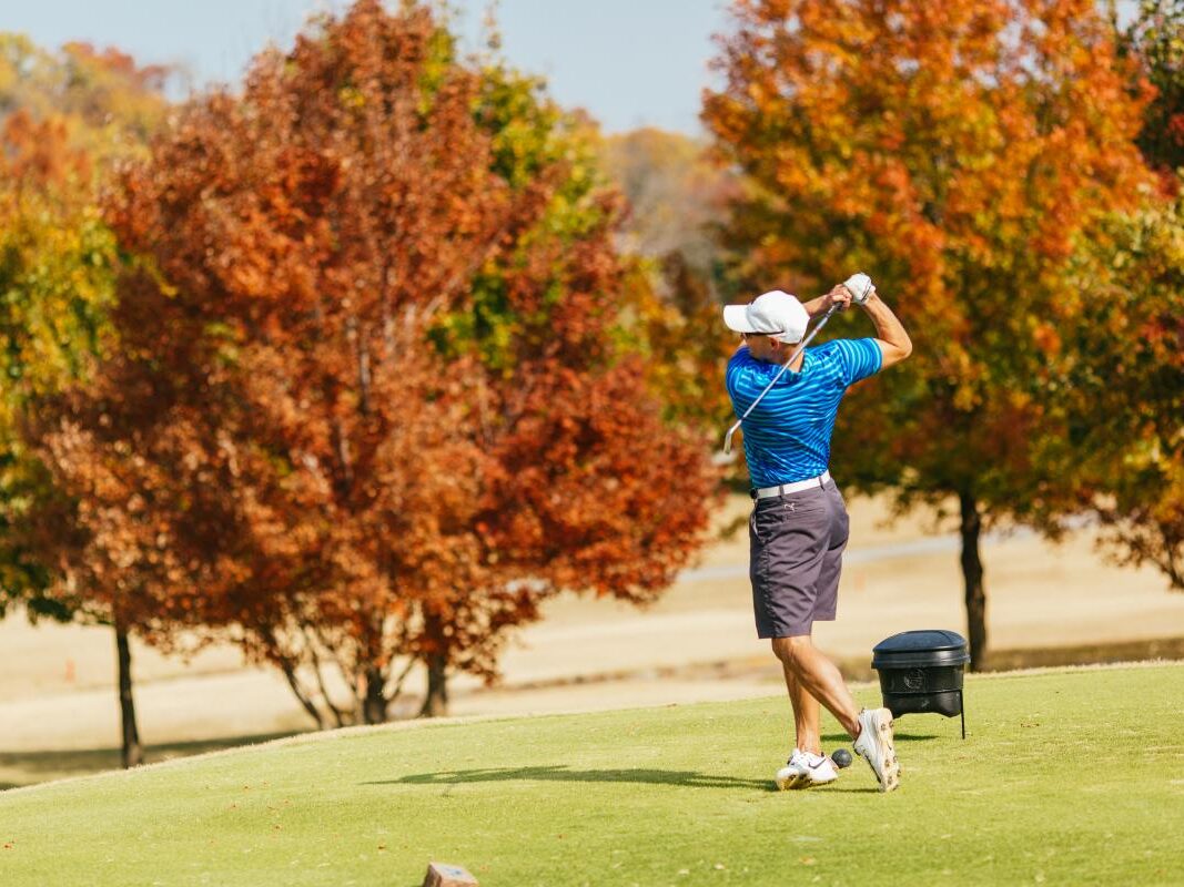 a man swinging a golf club in the fall.