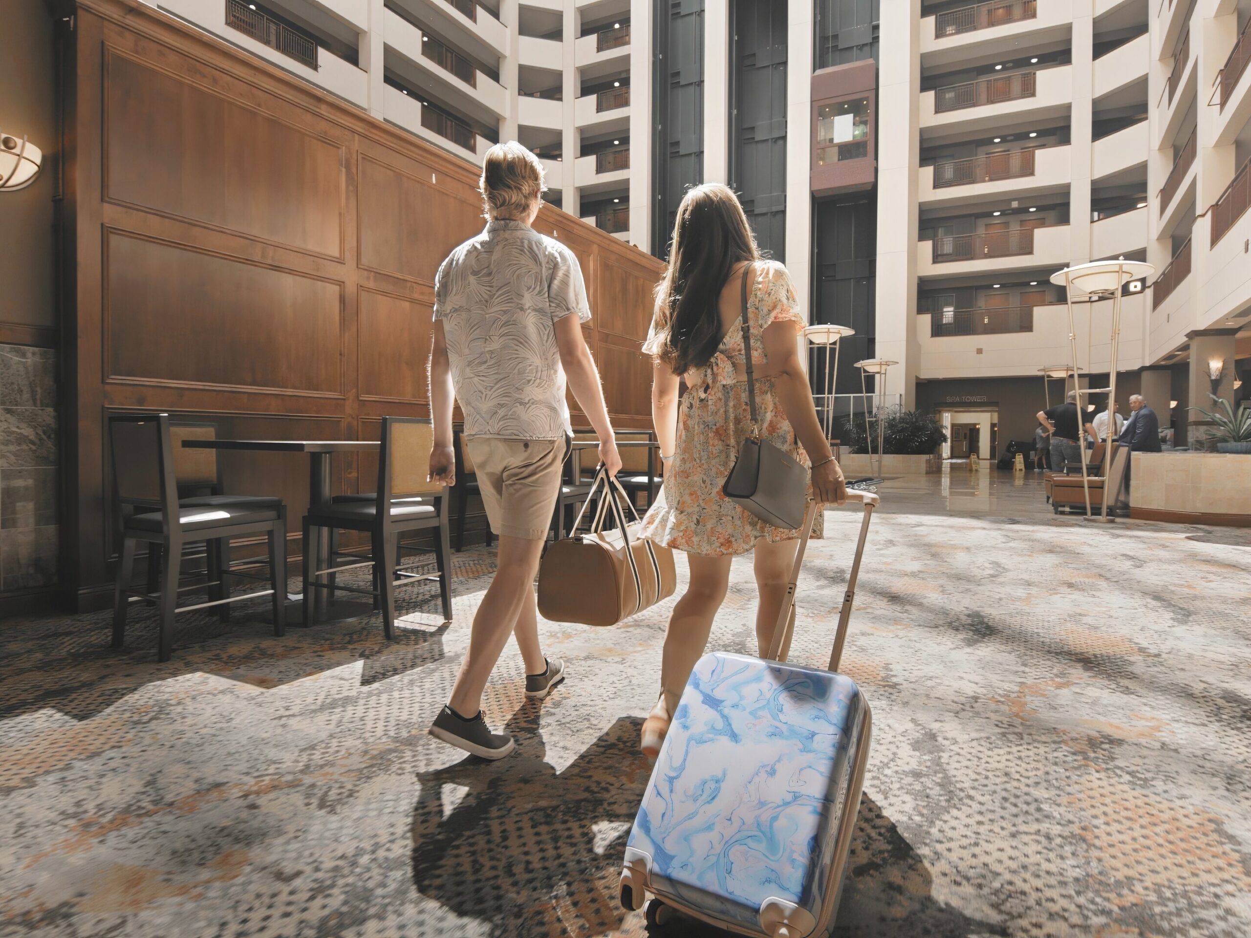 Two people walking through a hotel lobby with luggage.