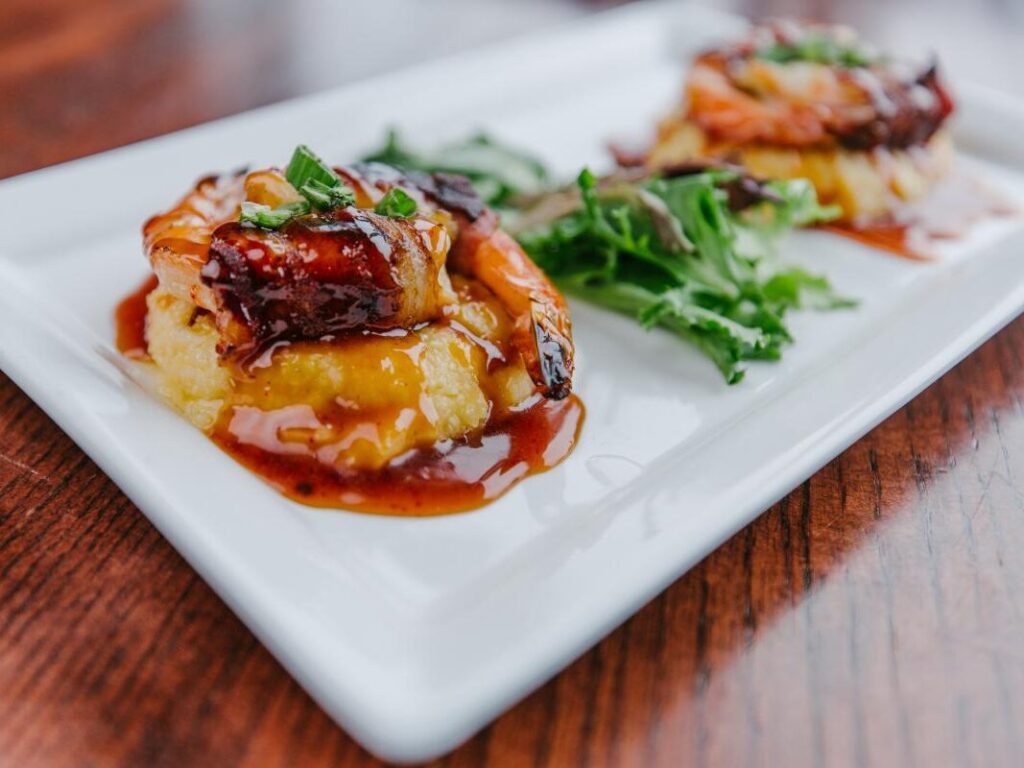 two shrimp on a plate with sauce and greens.