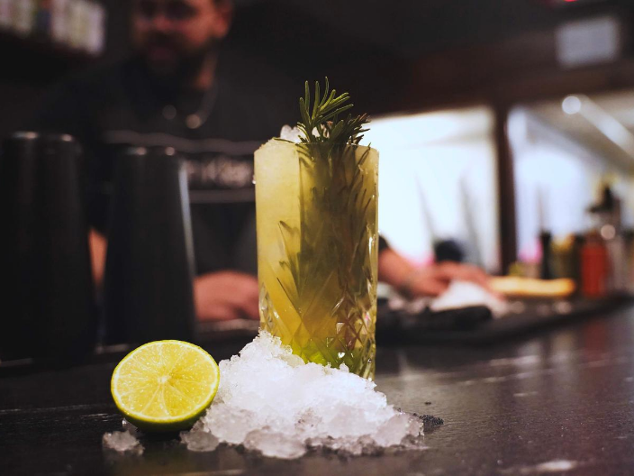 a cocktail with rosemary and ice on top of a bar.
