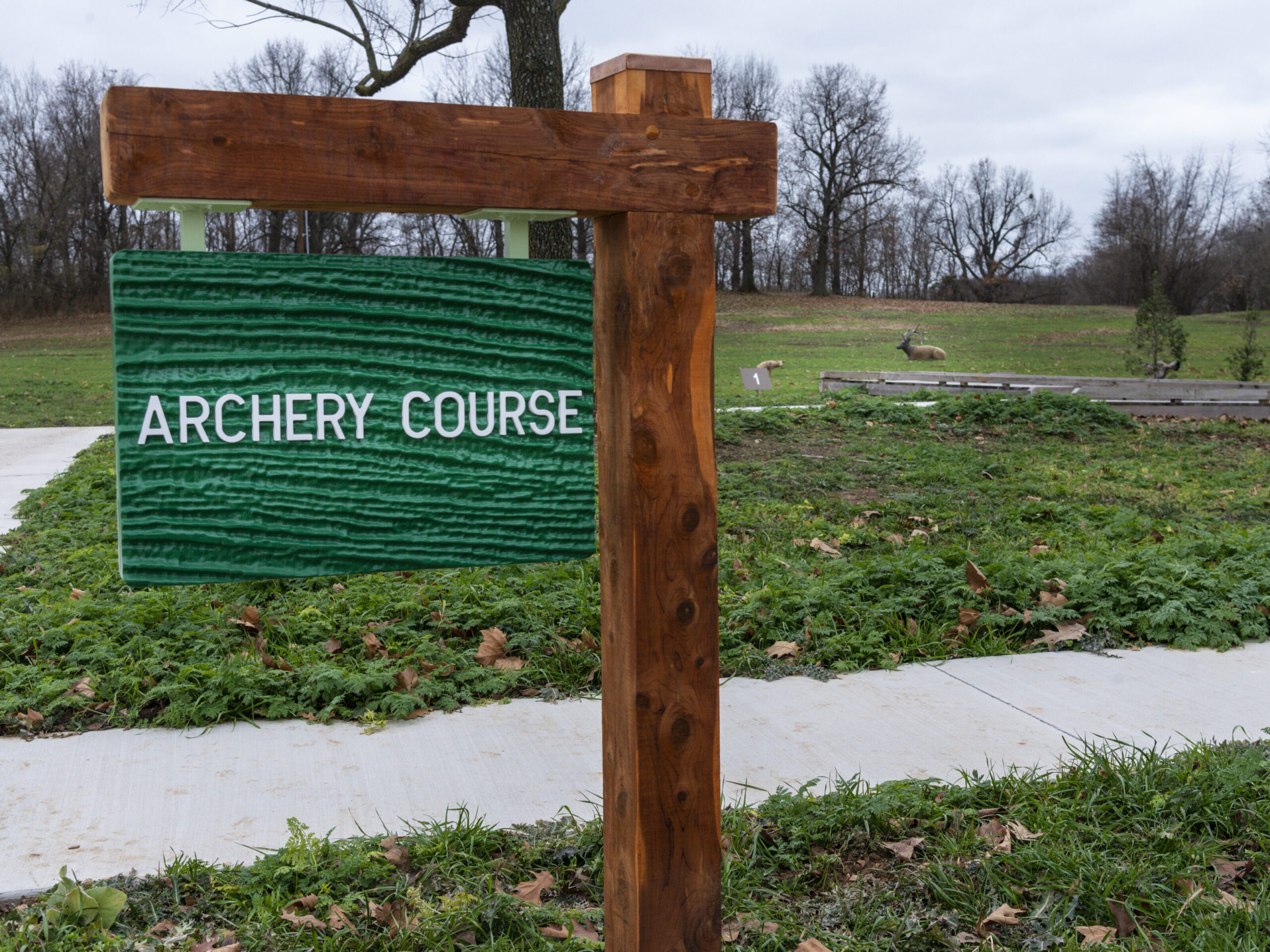 A wooden sign reads "Archery Course" in a grassy area with a path and distant archery targets.