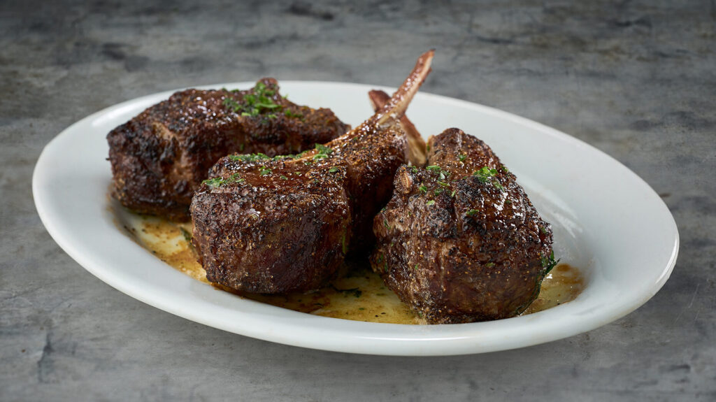 Lamb chops on a plate with sauce on it.