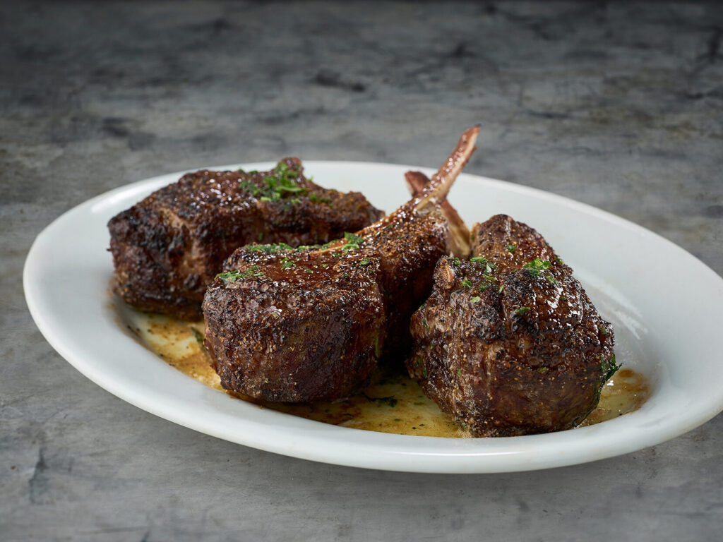 Lamb chops on a plate with sauce on it.
