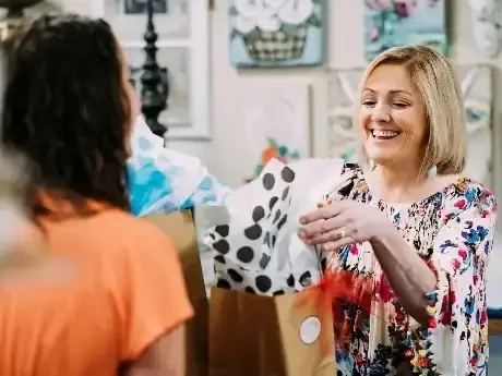 a woman is handing out gift bags to another woman.