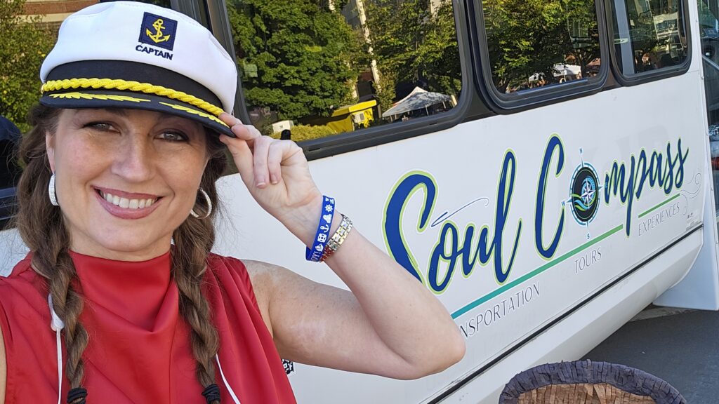 A woman in a captain's hat smiles and holds the brim, standing in front of a vehicle labeled "Soul Compass.