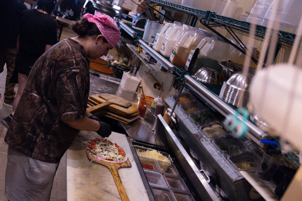 Employee builds pizza at The Rail - A Pizza Company inside kitchen.
