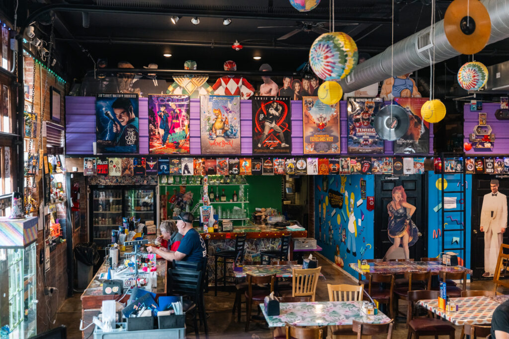Couple eats pizza at bar inside Flashback Pizza and Milkshakes surrounded by 80s and 90s memorabilia. 