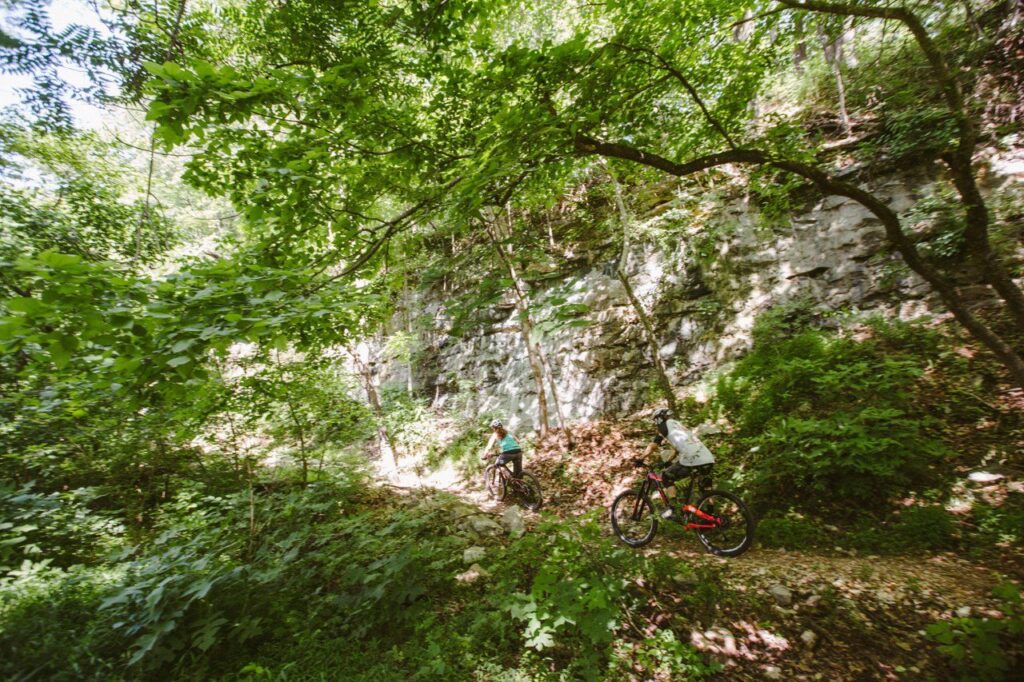 Mountain bikers riding Lake Atalanta's singletrack past a limestone bluff in Rogers, Arkansas